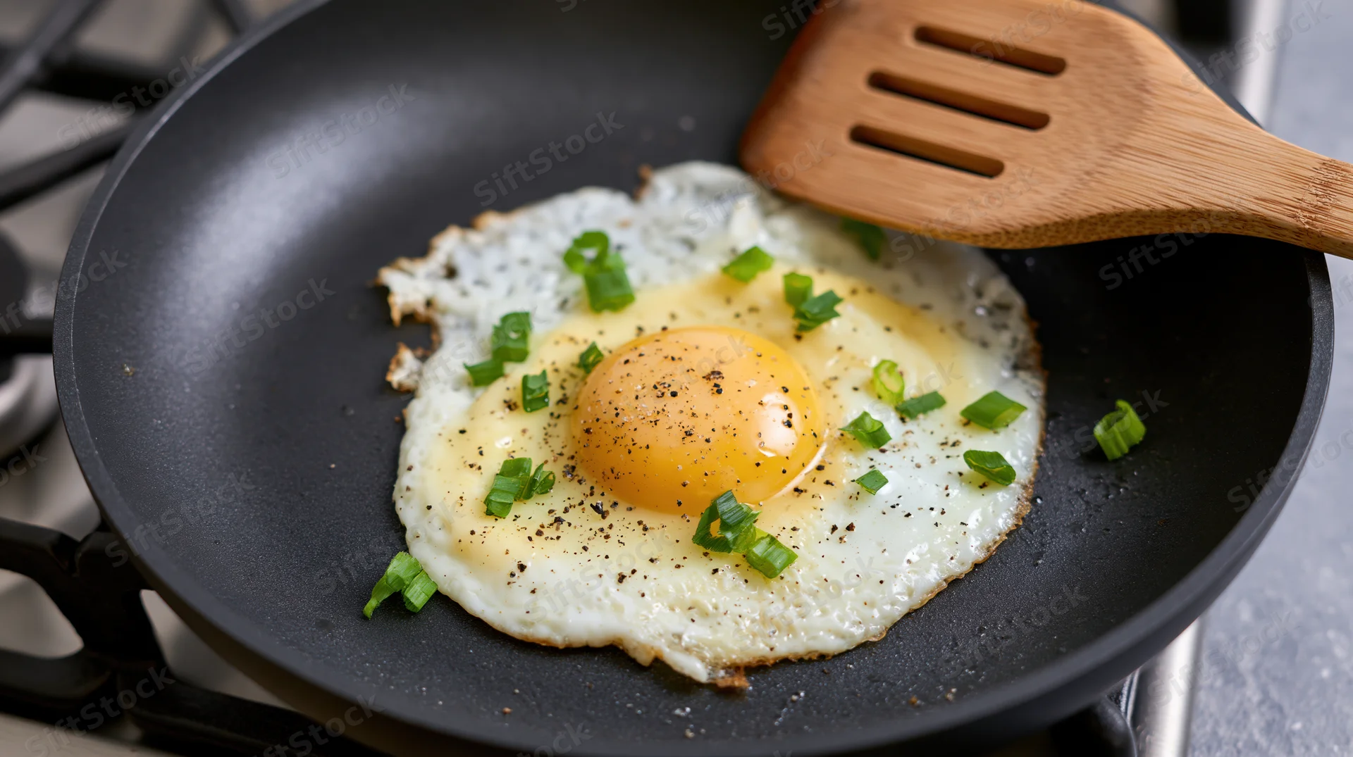 Sunny-side-up egg frying in a black nonstick skillet on a gas stove, garnished with green onions and pepper