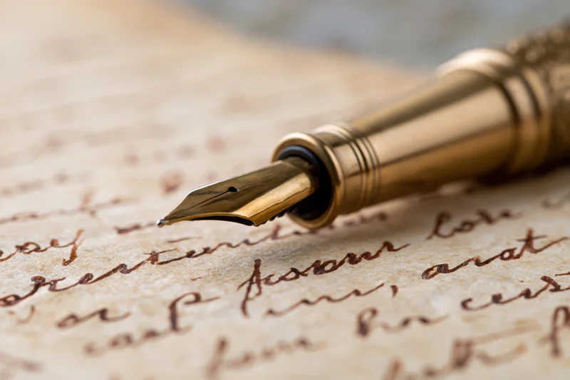 Gold fountain pen resting on aged handwritten letter with cursive script