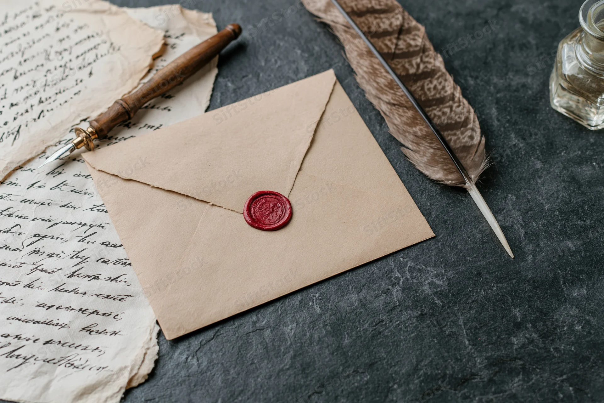 Kraft paper envelope with red wax seal lying on dark grey slate surface beside handwritten letter, quill pen and ink bottle