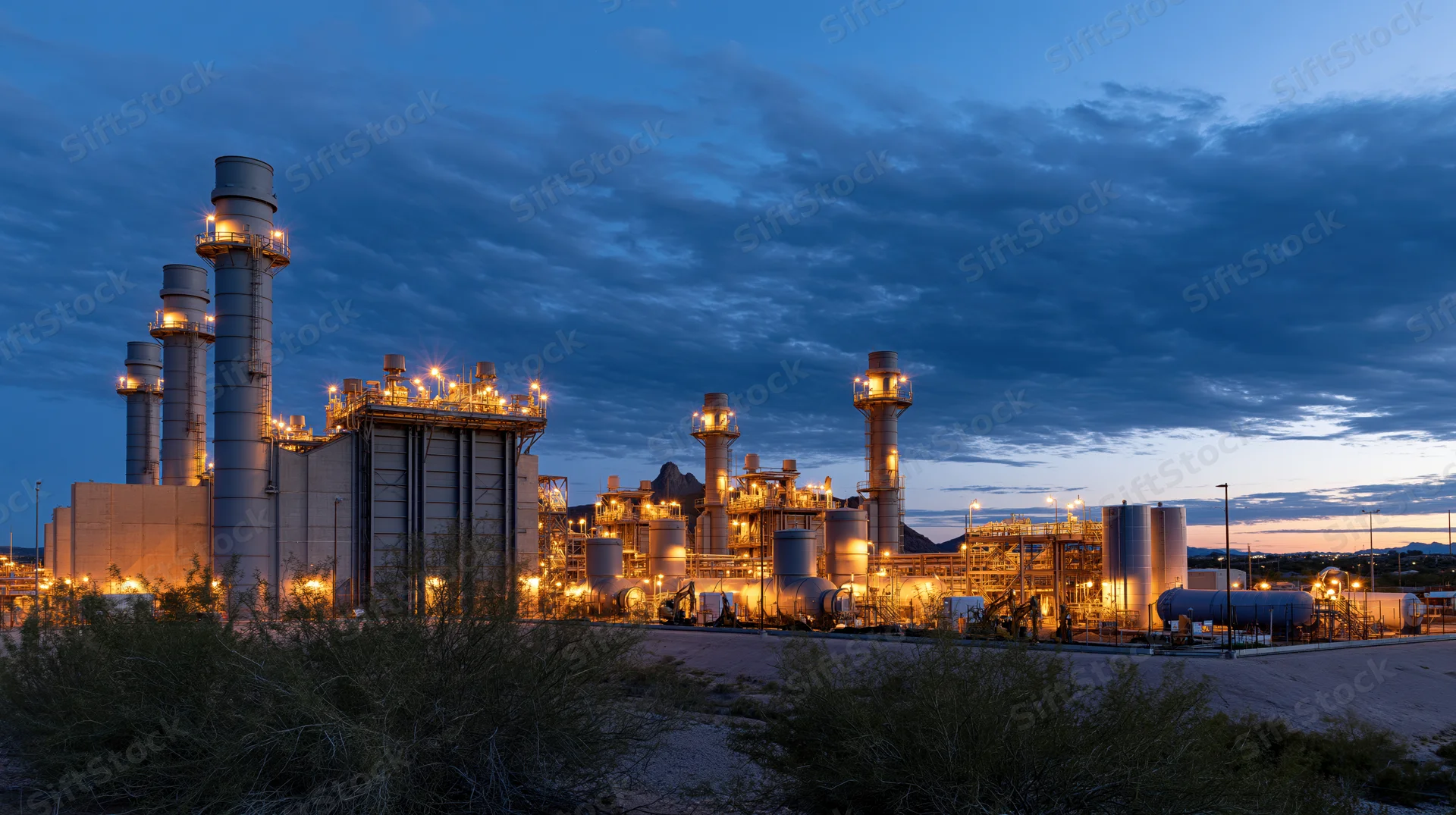 Large gas turbine power plant illuminated at dusk in desert landscape
