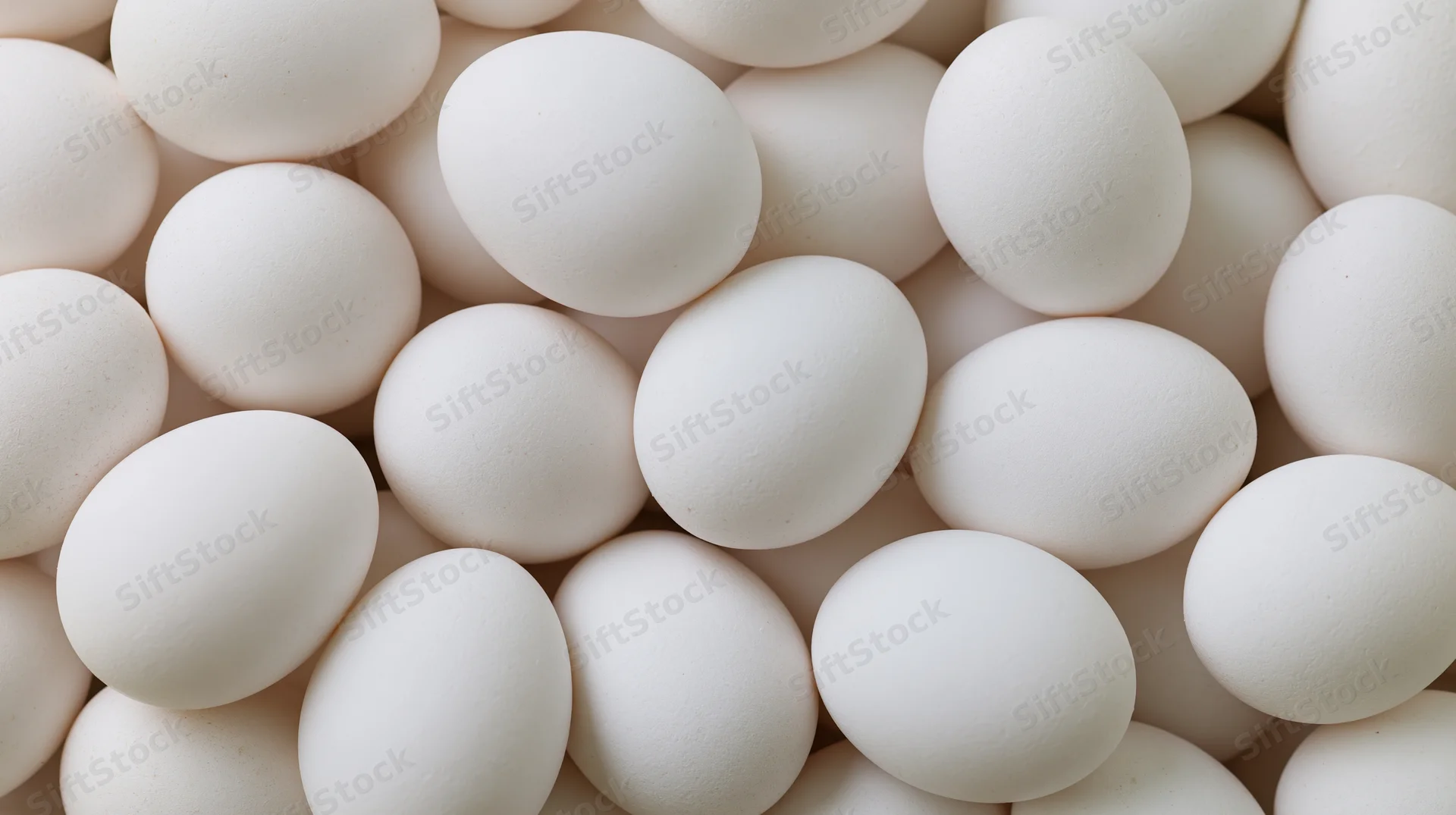 Closeup of white chicken eggs piled together filling the frame