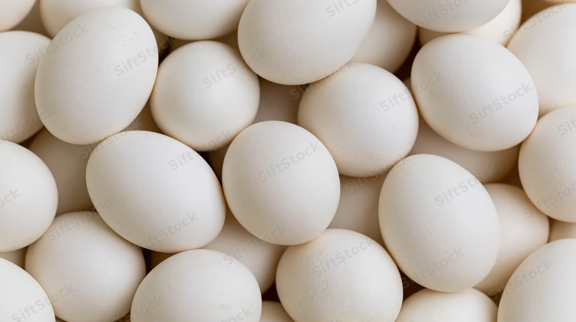 Closeup of white chicken eggs piled together filling the frame