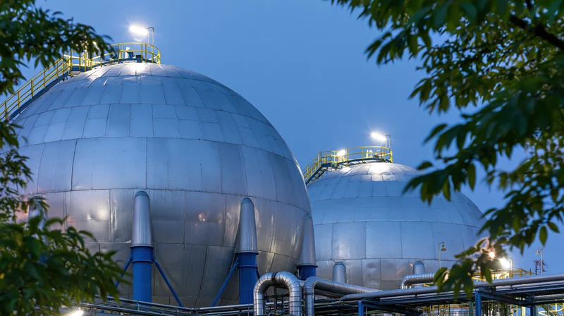 Large spherical steel gas storage tanks at a petrochemical facility with foliage in the foreground at evening