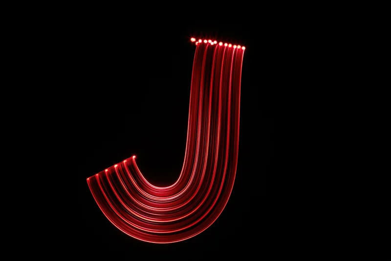 Red light trails forming lowercase letter j against black background