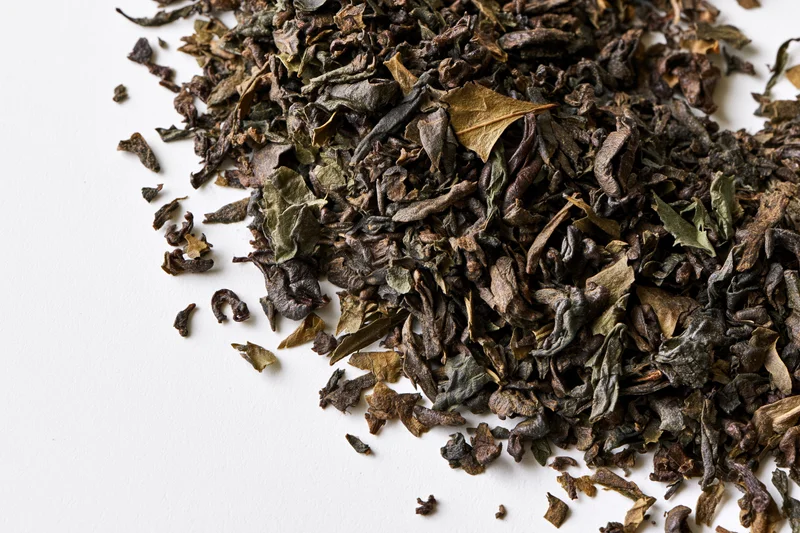 Loose dried tea leaves scattered in a diagonal swirl on a white surface