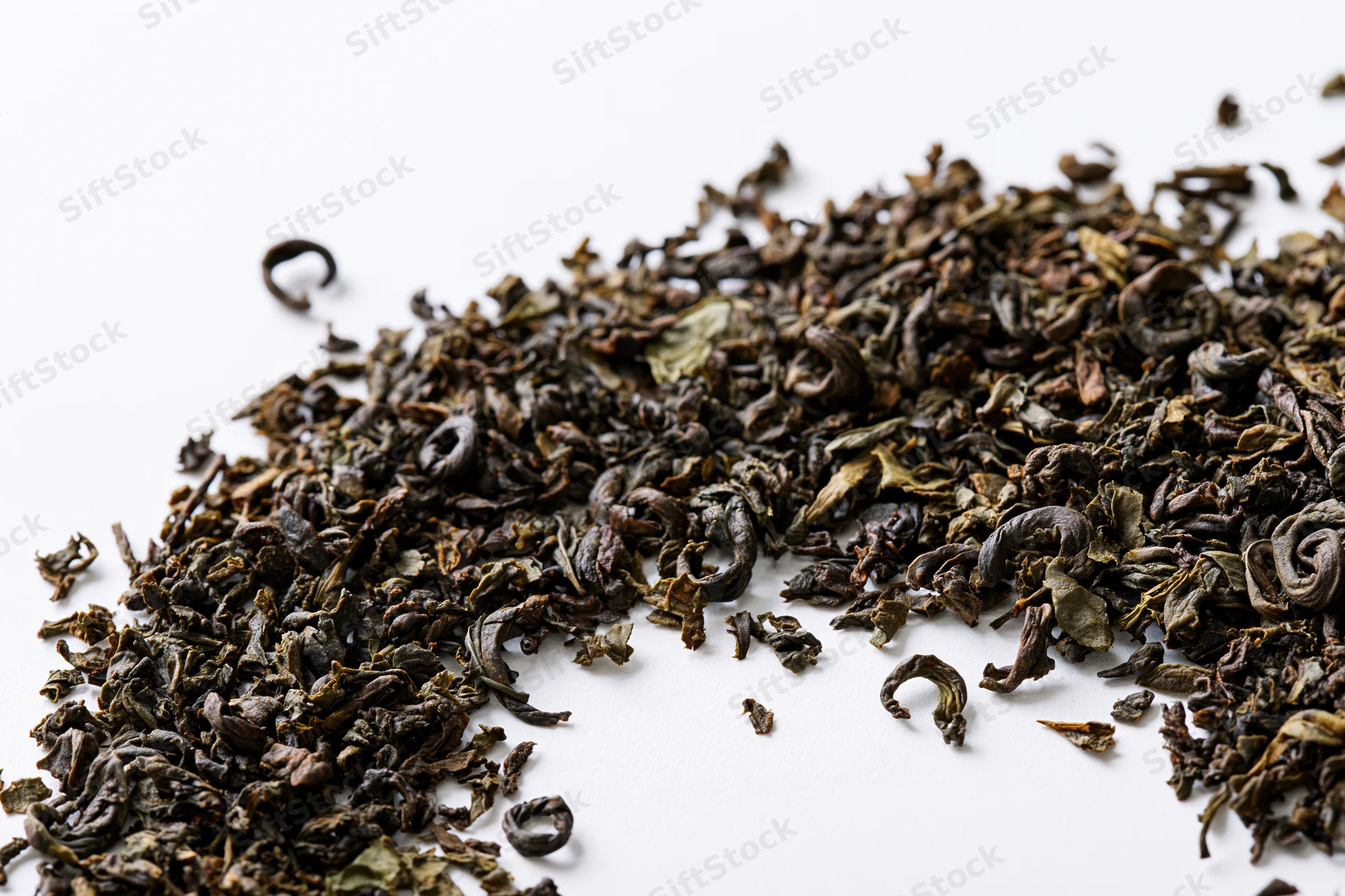 Loose dried tea leaves scattered in a diagonal swirl on a white background