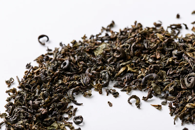 Loose dried tea leaves scattered in a diagonal swirl on a white background