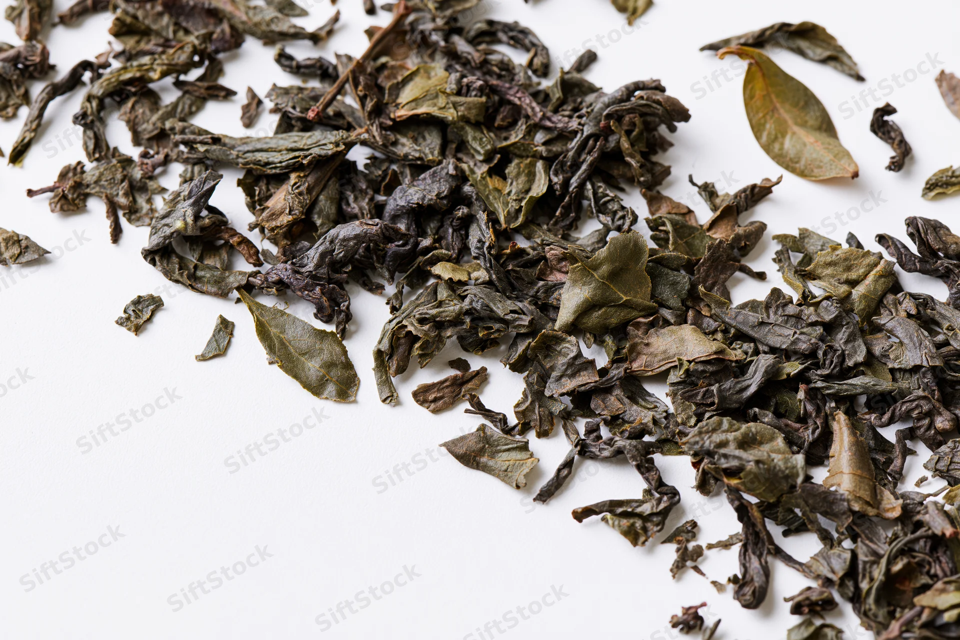 Dried tea leaves scattered in a diagonal swirl on white background