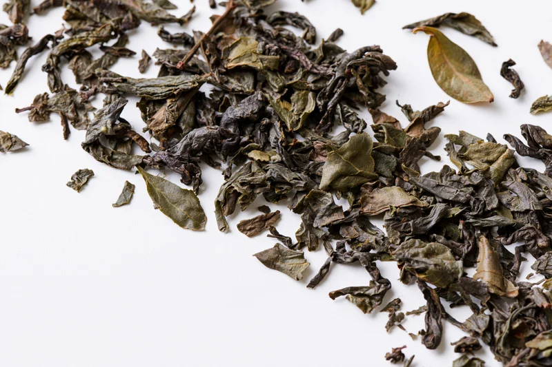 Dried tea leaves scattered in a diagonal swirl on white background