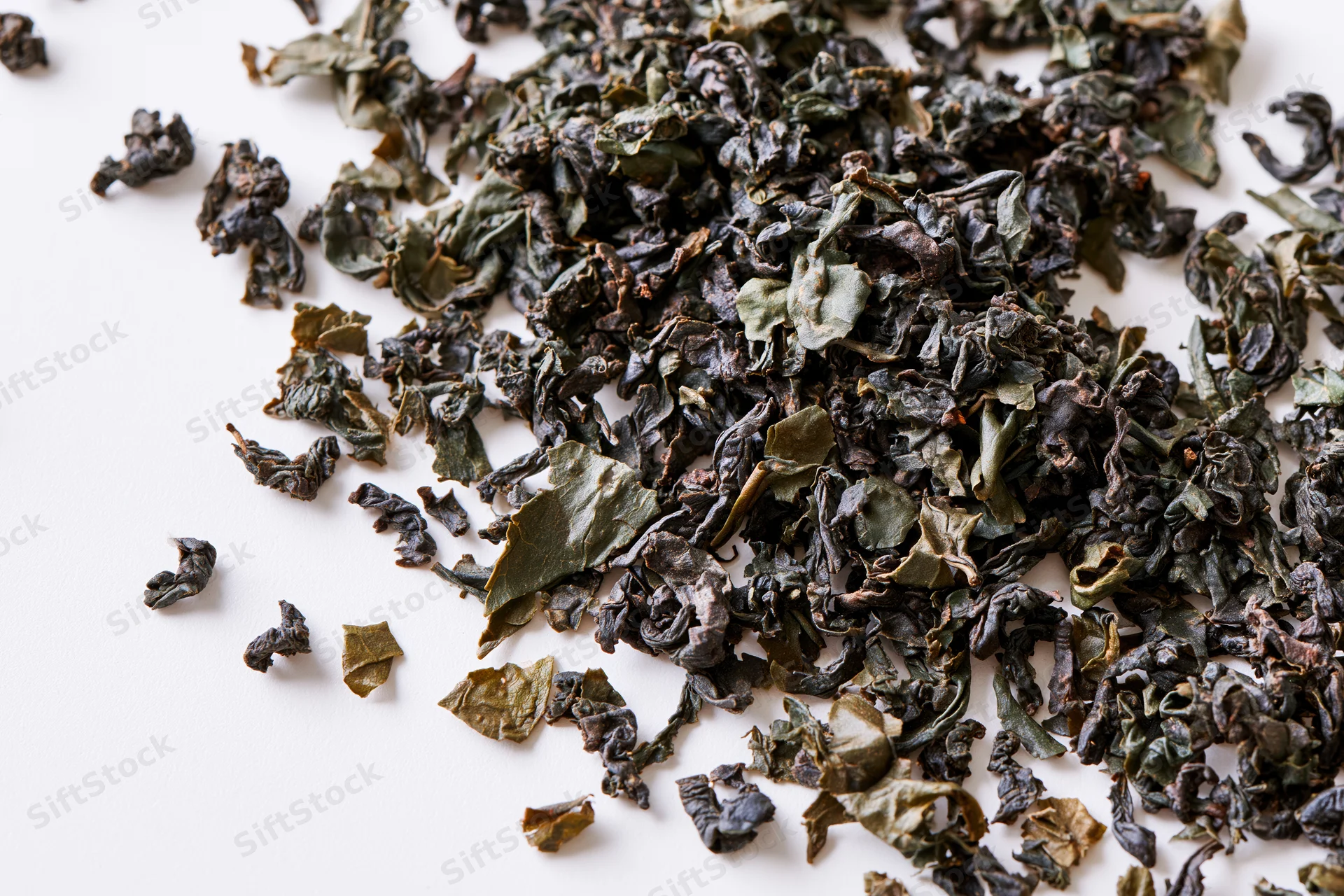 Loose dried tea leaves scattered in a diagonal swirl on white surface