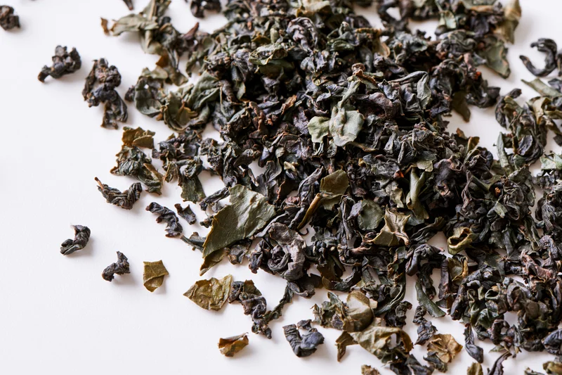 Loose dried tea leaves scattered in a diagonal swirl on white surface