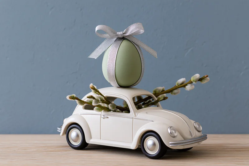Miniature white vintage toy car with green easter egg and willow branches on wooden surface