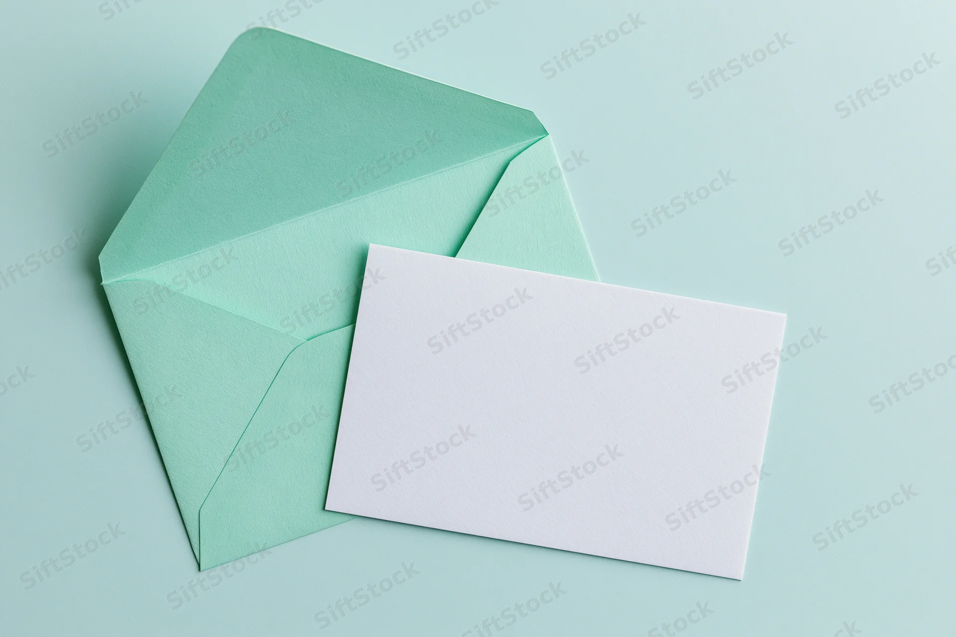 Mint green envelope with open flap overlapping a blank white card on a light green background