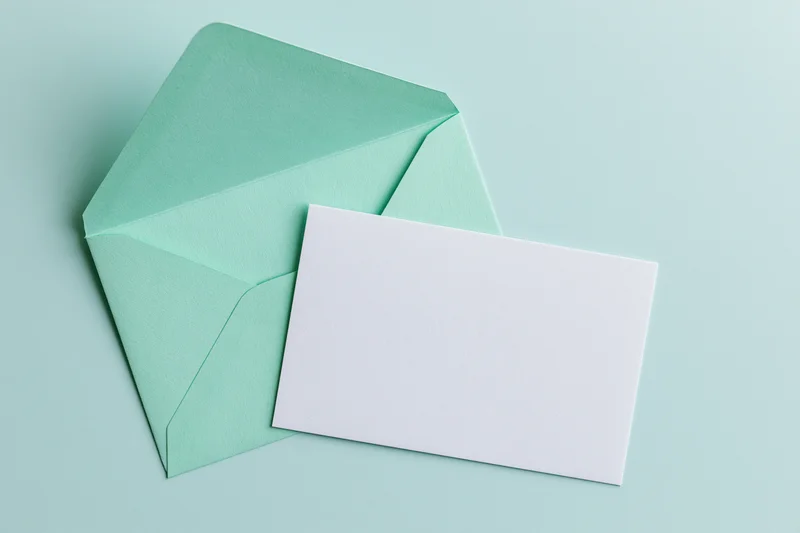 Mint green envelope with open flap overlapping a blank white card on a light green background