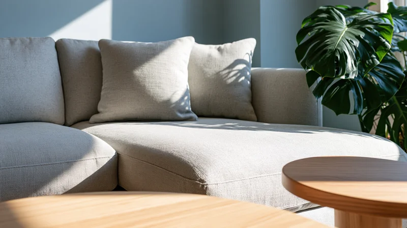 Light grey linen sectional sofa in a modern living room corner with sunlight and a monstera plant