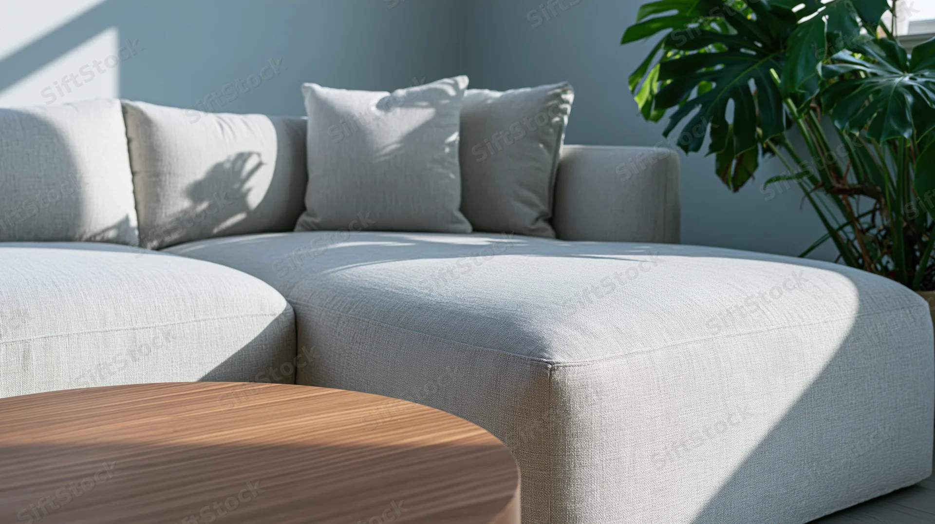 Light grey linen sectional sofa in a modern living room corner with a round wooden coffee table and a monstera plant