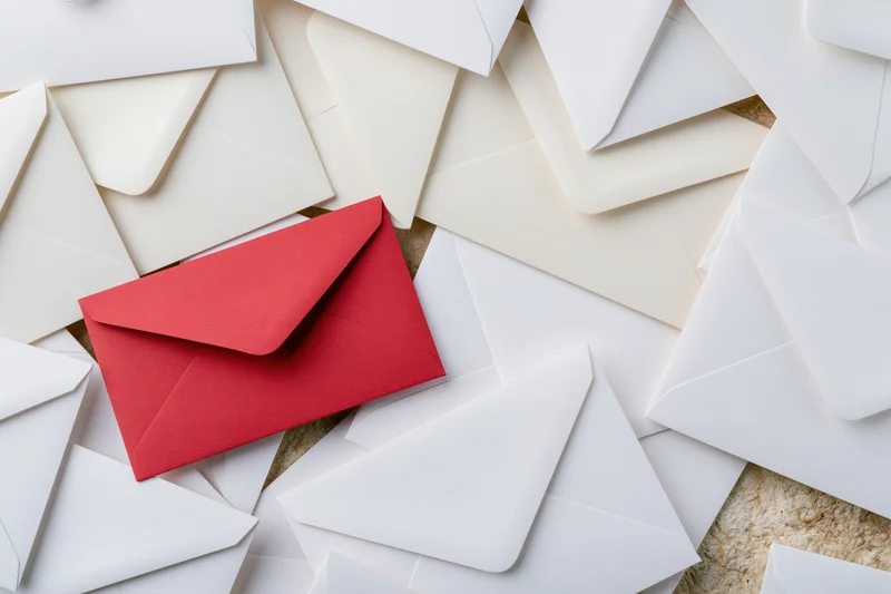 Red envelope among scattered white envelopes on textured surface