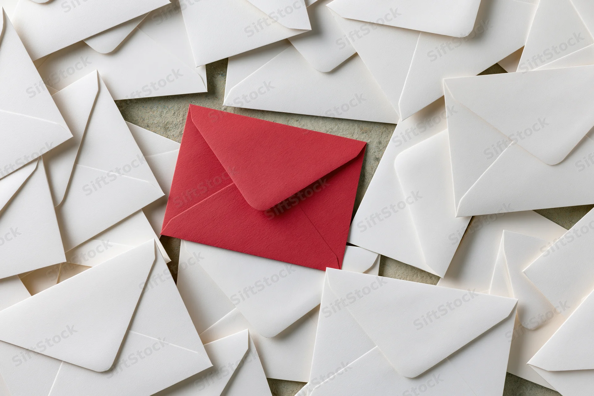 Red envelope among scattered white envelopes on textured surface