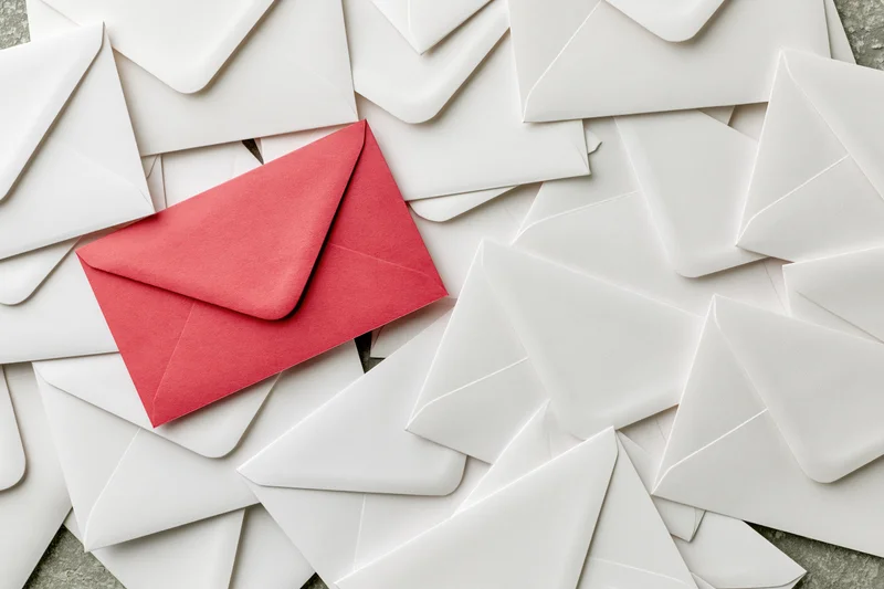 Red envelope among scattered white envelopes on textured surface