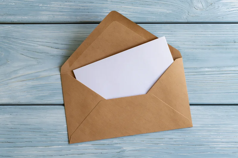 Open kraft envelope with blank white card on blue wooden surface