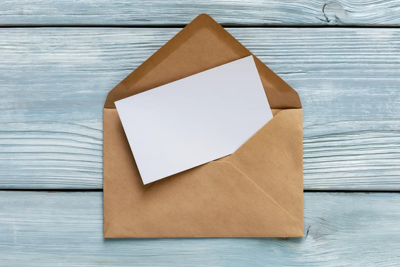 Open kraft envelope with blank white card on blue wooden surface