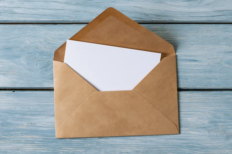 Open kraft paper envelope with blank white card on blue wooden surface