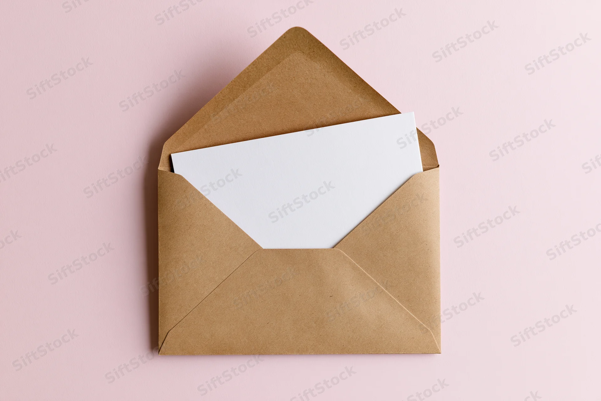 Open kraft paper envelope with blank white card on pink background