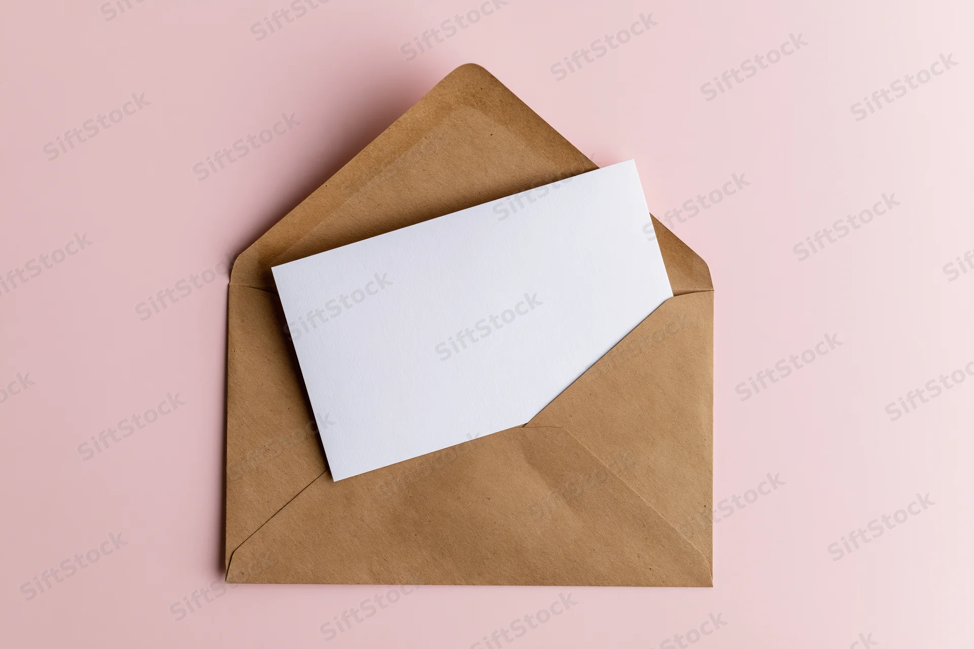 Open kraft paper envelope with blank white card on pink background