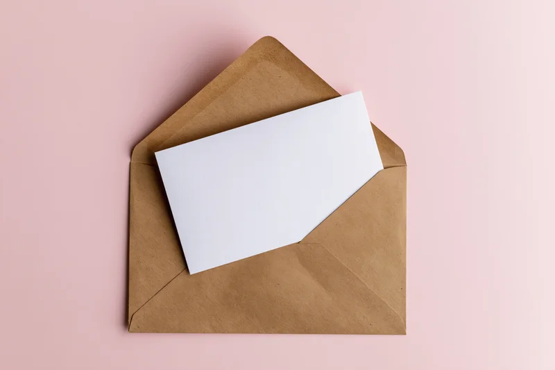 Open kraft paper envelope with blank white card on pink background