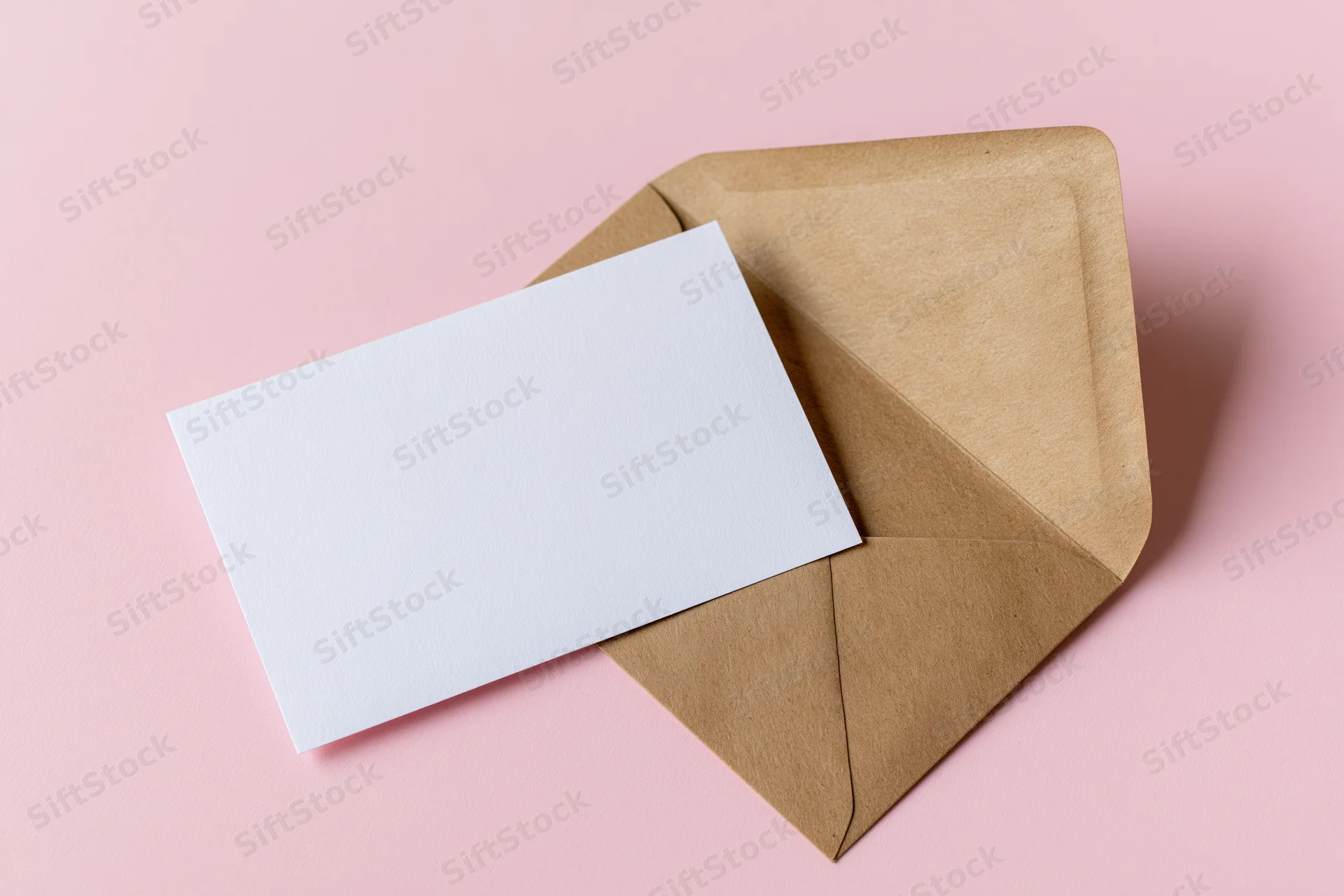 Open kraft envelope with blank white card on pink background