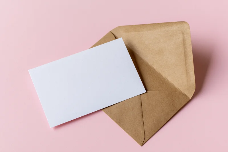 Open kraft envelope with blank white card on pink background