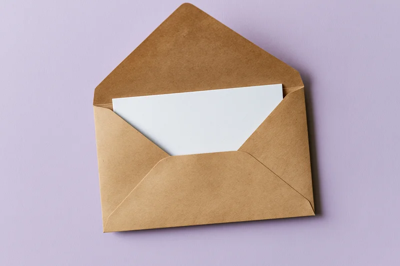Open kraft paper envelope with blank white card on purple background