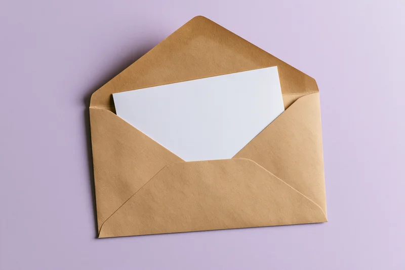 Open kraft paper envelope with blank white card inside on lavender background
