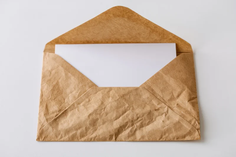 Open kraft paper envelope with blank white card inside on white surface