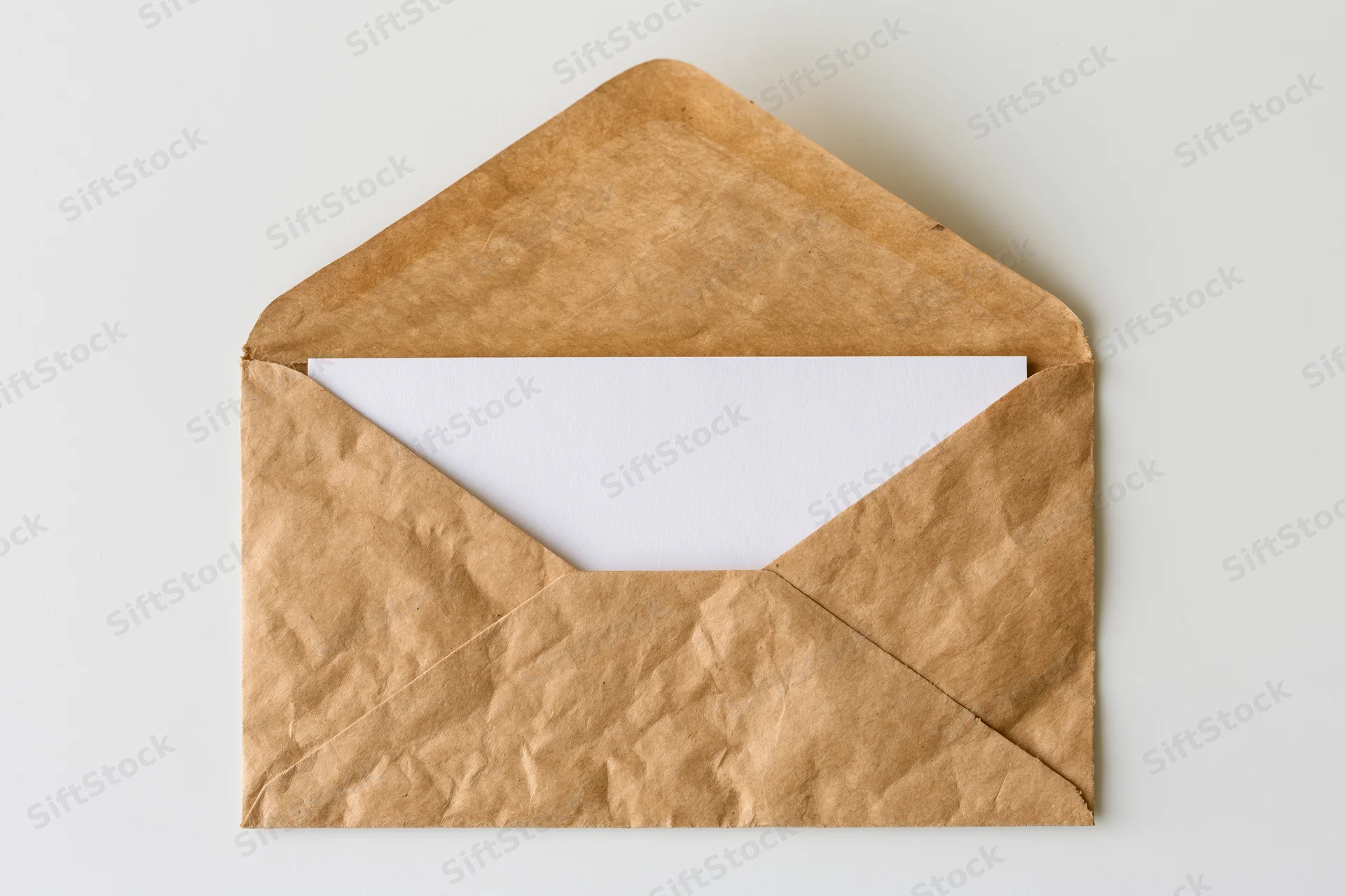 Open kraft paper envelope with blank white card inside on white surface