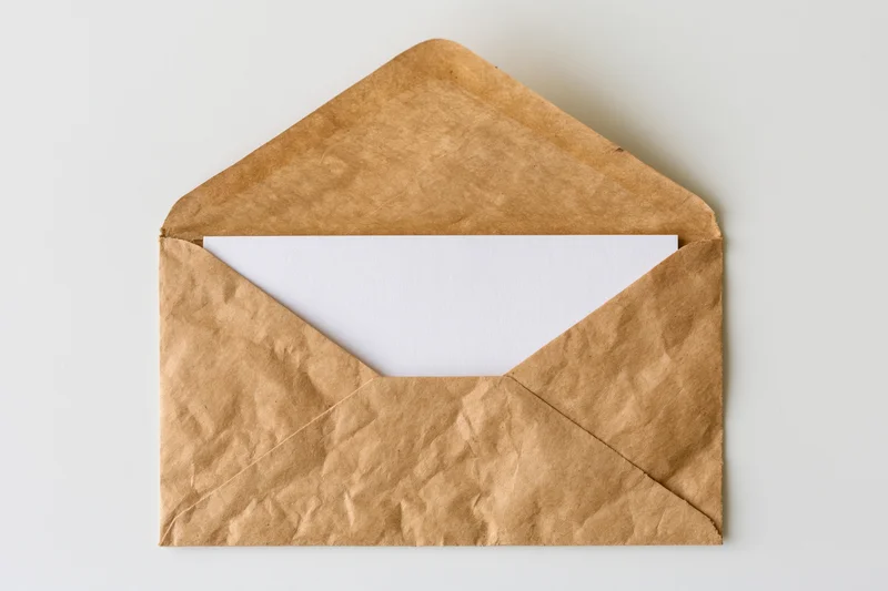 Open kraft paper envelope with blank white card inside on white surface
