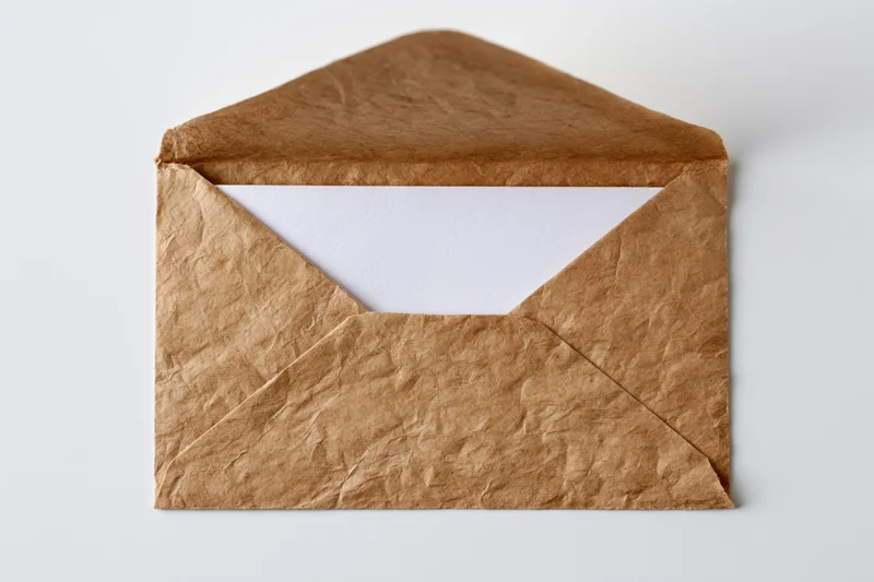 Open kraft paper envelope with blank white card inside on white background