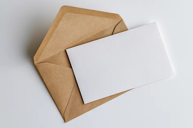 Open kraft paper envelope with blank white card resting on white surface