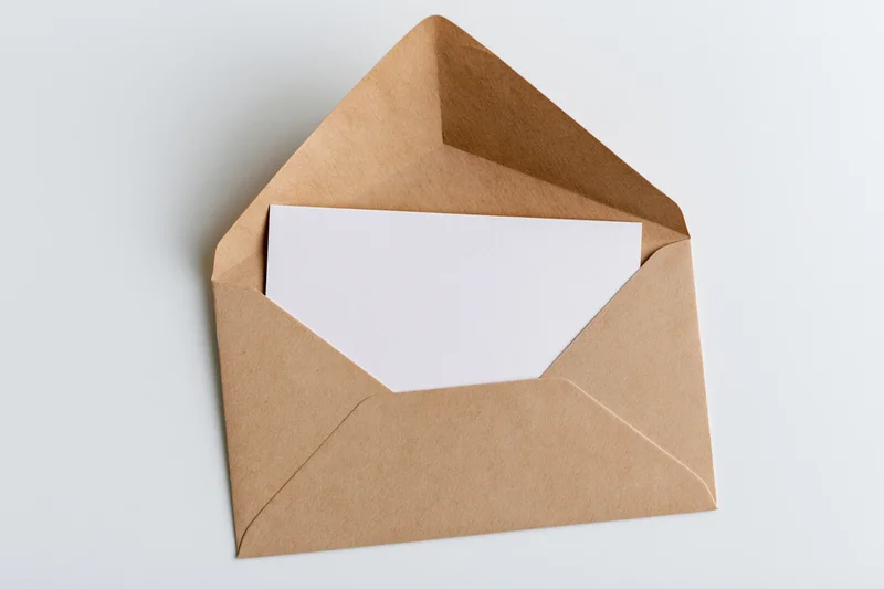 Open kraft paper envelope with blank white card inside on white surface