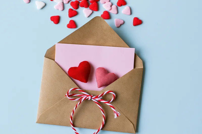 Open kraft envelope with pink note and felt hearts on light blue surface
