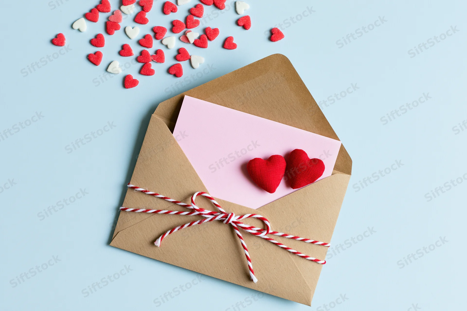 Open kraft envelope with pink note and red hearts tied with string on light blue background