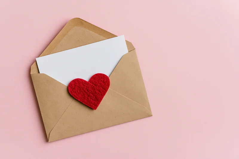 Open kraft envelope with red felt heart sticker on pink background