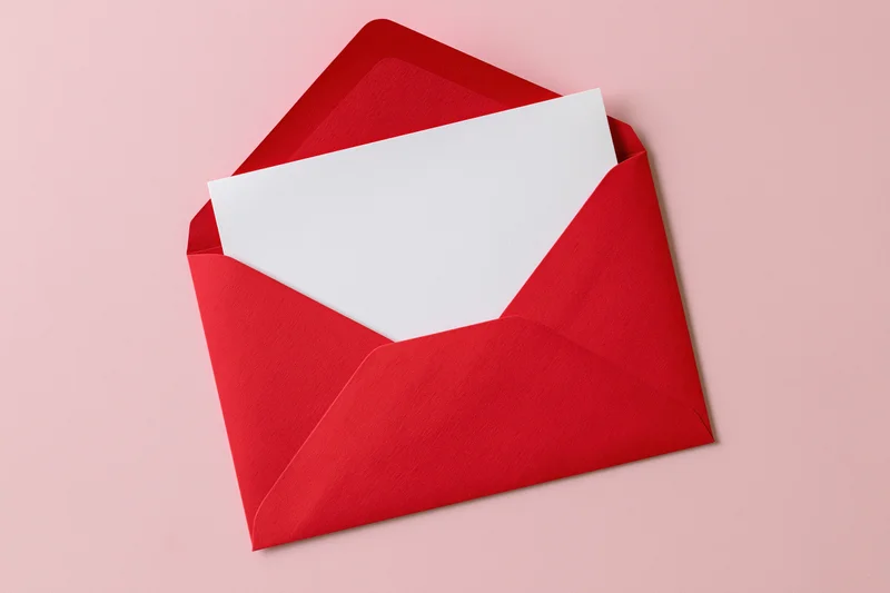 Open red paper envelope with blank white card inside on pink surface
