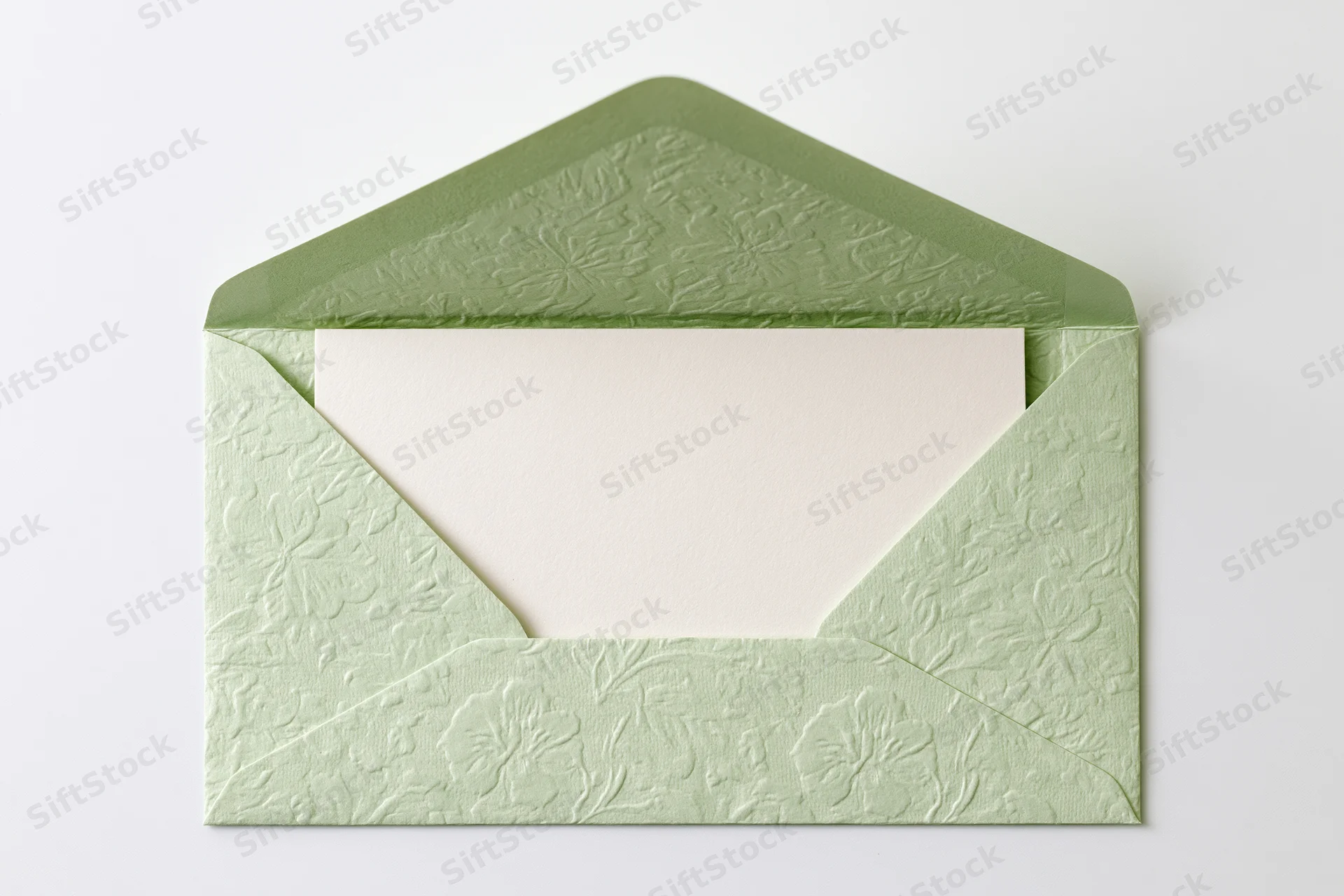 Open sage green embossed floral envelope holding blank card on white background