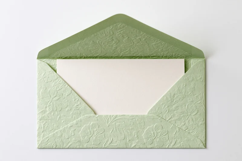 Open sage green embossed floral envelope holding blank card on white background