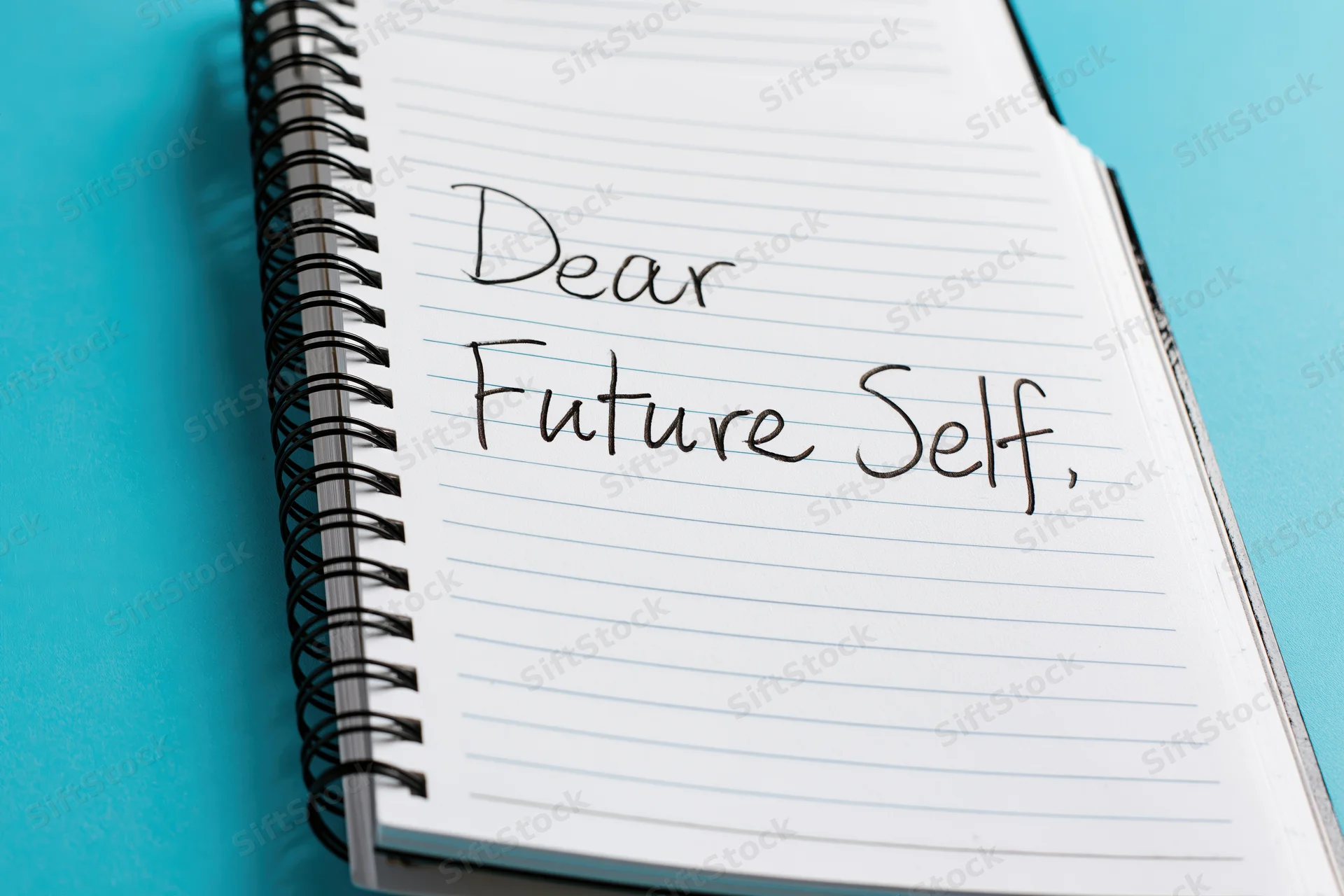Spiral-bound notebook open to page with handwritten cursive text reading "Dear Future Self" on lined paper against blue background
