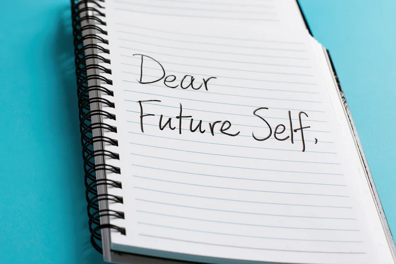 Spiral-bound notebook open to page with handwritten cursive text reading "Dear Future Self" on lined paper against blue background