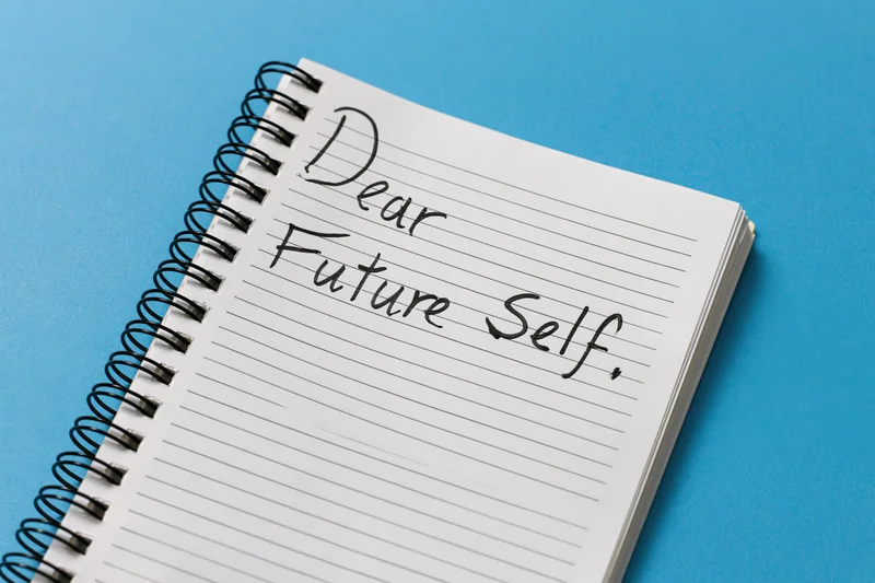 Spiral-bound notebook with handwritten cursive text reading "Dear Future Self" on lined paper against blue background