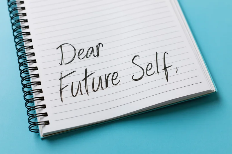 Spiral-bound notebook with handwritten cursive text reading "Dear Future Self" on lined paper against a blue background