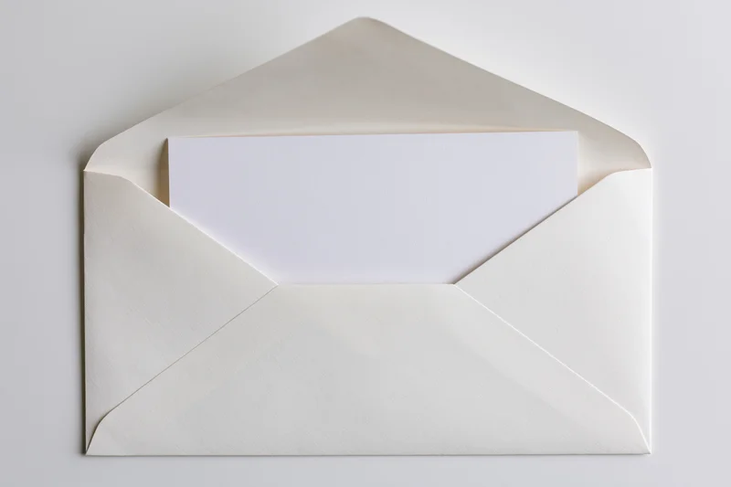 Open white envelope with blank card partially pulled out on plain surface